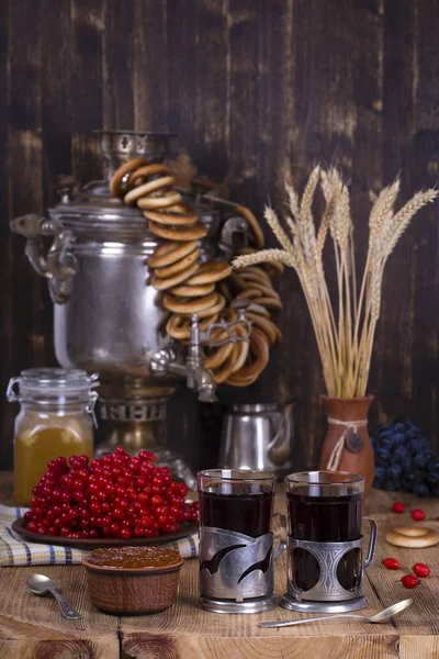 Der traditionelle russische Wasserkocher Samowar auf dem Holztisch. Schwarztee, Bagels, rotes Viburnum, Marmelade und russischer Samowar im rustikalen Stil. — Stockfoto