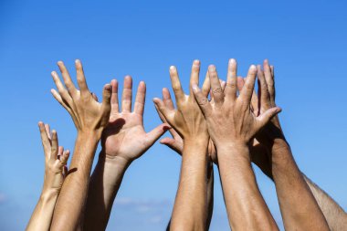 Group raising hands against blue sky background, close up clipart