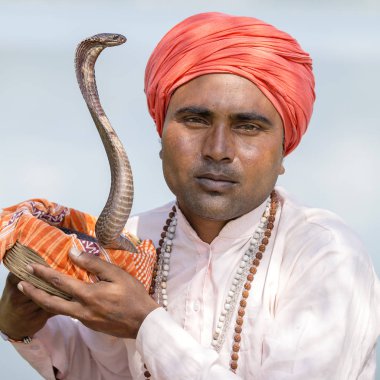 Portrait of snake charmer adult man in turban and cobra sitting near the lake in Pokhara, Nepal clipart