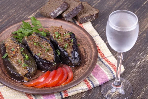 Baked eggplant stuffed with onions, cherry plums, walnuts on the plate and a glass of cold vodka — Stock Photo, Image