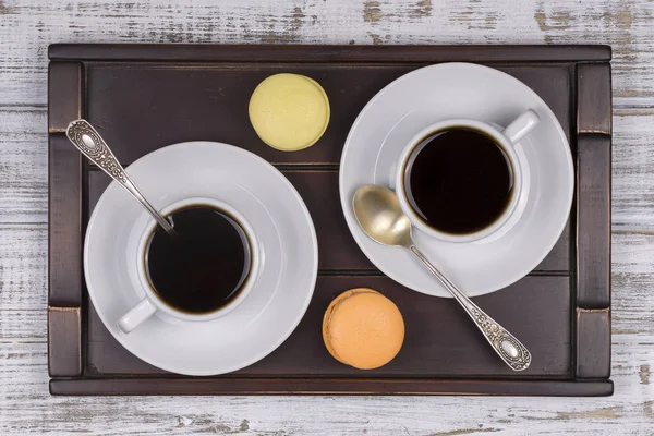 Deux tasses de café, cuillère et gâteaux de macaron sur un plateau sur une table en bois blanc. Concept de style de vie. Gros plan — Photo