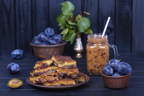 Hemmagjord plommon paj i plattan, plommon smoothies och raw blå plommon på svart trä bakgrund, — Stockfoto