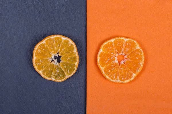 Slices of mandarin lies on orange napkin and on black slate. Concept of healthy, organic, vegan food, vitamins. Top view. Fresh orange, tangerine background