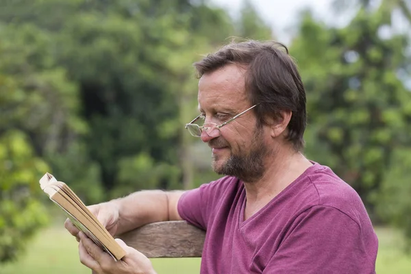 Portrait d'un homme caucasien de cinquante ans lisant un livre en plein air dans un parc lors d'une journée d'été ensoleillée — Photo