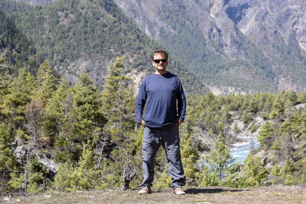 Mann mittleren Alters steht an einem sonnigen Sommertag in der Nähe blauer Fluss- und Berglandschaft im Himalaya — Stockfoto