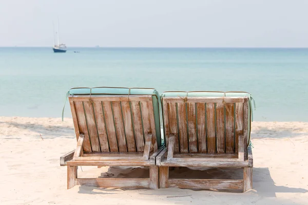 Пара деревянных пляжных стульев на тропическом песчаном пляже с видом на морскую воду и яхту. Таиланд — стоковое фото