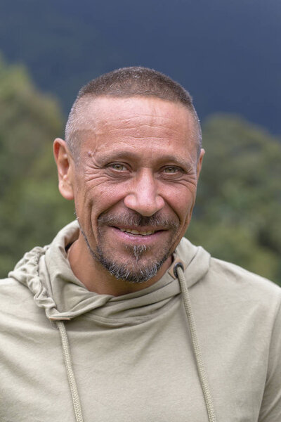 People and lifestyle concept. Happy middle-aged unshaven man with cheerful smile outdoor against green nature background, portrait close up