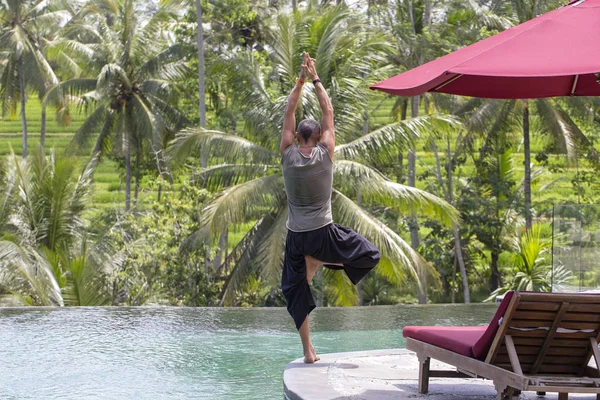 Man doing yoga and meditating in tree position near swimming pool on island Bali, Indonesia