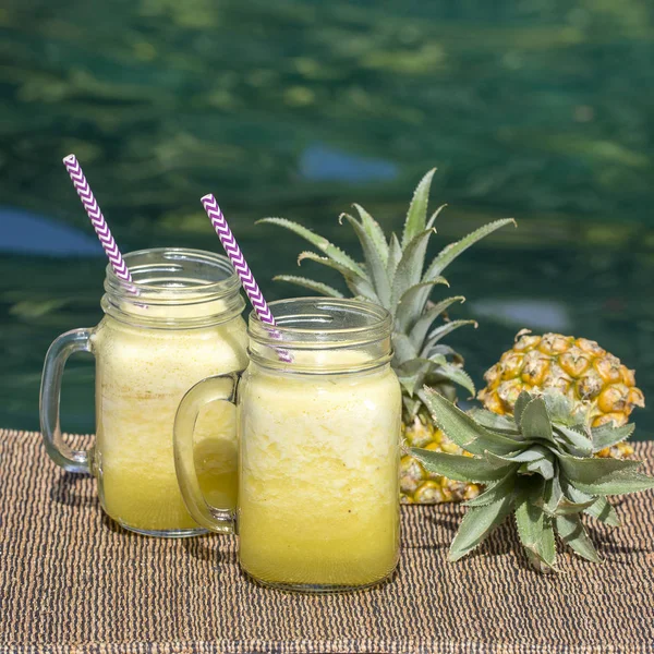 Hemlagad mango och ananas smoothie gjord på kokosmjölk i två glas mugg nära poolen, närbild. Uppfriskande tropisk fruktdrink — Stockfoto