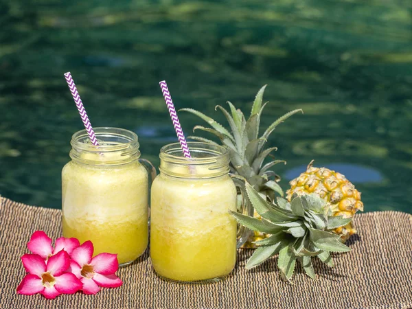 Batido casero de mango y piña hecho con leche de coco en dos jarras de vidrio cerca de la piscina, de cerca. Refrescante bebida de frutas tropicales — Foto de Stock