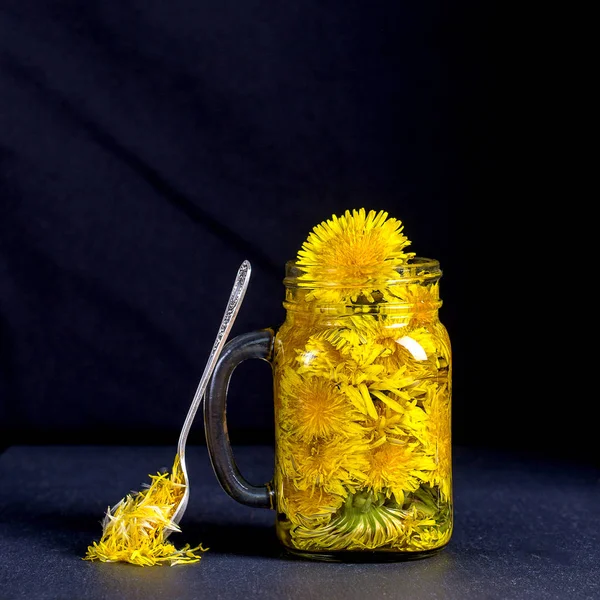 Bebida de chá de flor amarela de dente de leão em caneca de vidro no fundo preto. Conceito de alimentação saudável — Fotografia de Stock