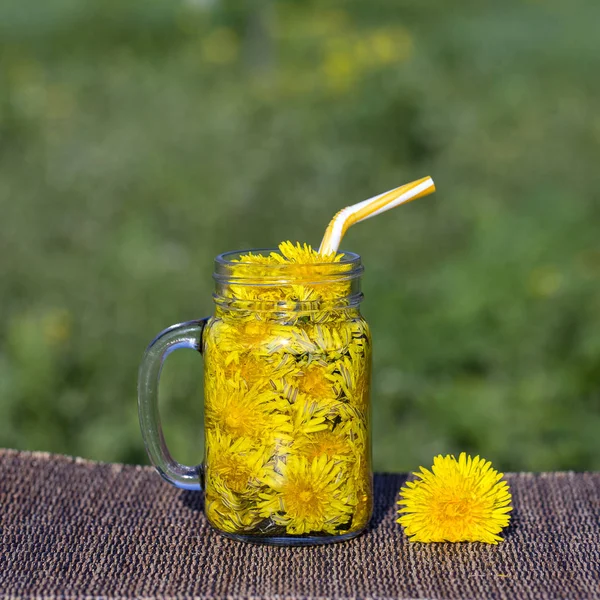 Diente de león amarillo flor té bebida en taza de vidrio en la mesa, al aire libre. Concepto de alimentación saludable —  Fotos de Stock