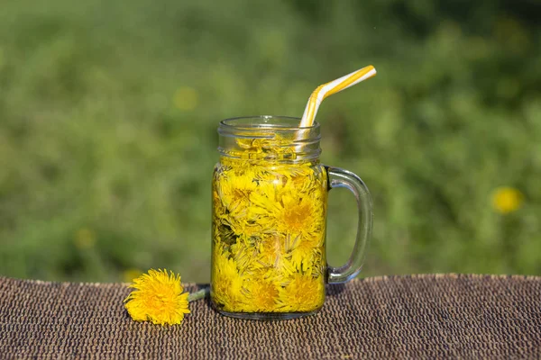 Dandelion yellow flower tea drink in glass mug on table, outdoors. Concept of healthy eating