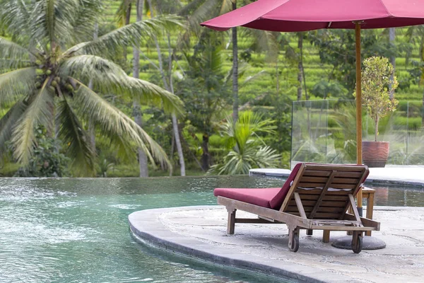 Guarda-chuva vermelho e cadeiras de praia em torno da piscina exterior no hotel e resort com palmeira na ilha Bali, Indonésia — Fotografia de Stock
