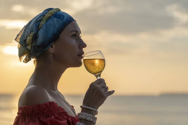 Mujer mano sosteniendo copa de vino contra una hermosa puesta de sol cerca del mar en la playa tropical, de cerca — Foto de Stock