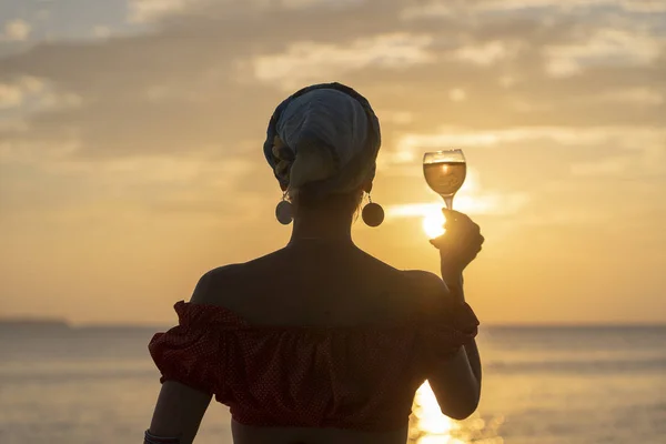 Mujer mano sosteniendo copa de vino contra una hermosa puesta de sol cerca del mar en la playa tropical, de cerca — Foto de Stock