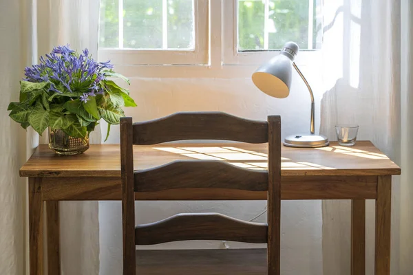 Дерев'яний стіл зі стільцем, лампа і букет квітів біля вікна в сучасній робочій зоні будинку — стокове фото