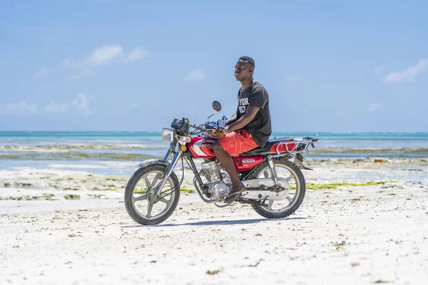 Africano monta uma motocicleta em uma praia de areia na maré baixa na ilha de Zanzibar, Tanzânia, África Oriental — Fotografia de Stock