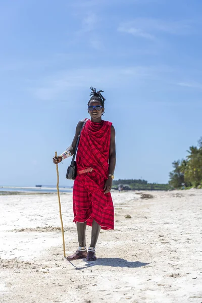 Afrikaanse man masai gekleed in traditionele kleren staan in de buurt van de oceaan op het zandstrand, Zanzibar, Tanzania — Stockfoto