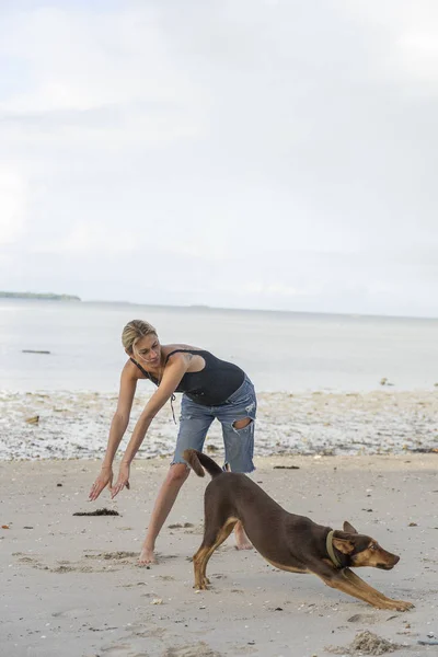 Mujer joven con un perro hacer fitness cerca de agua de mar en la playa tropical en la isla de Zanzíbar, Tanzania, África —  Fotos de Stock