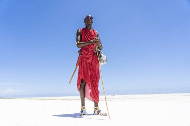 Afrikalı adam geleneksel kıyafetler giyip okyanusun kenarında, kumsalda, Zanzibar, Tanzanya 'da duruyor.