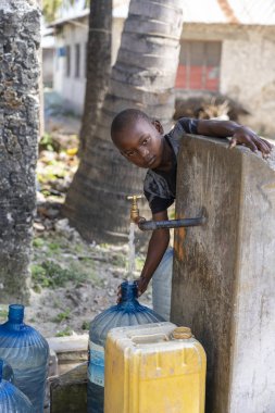 Afrikalı çocuk kutuyu Doğu Afrika 'daki Zanzibar Adası' ndaki bir sokakta musluk suyuyla dolduruyor.