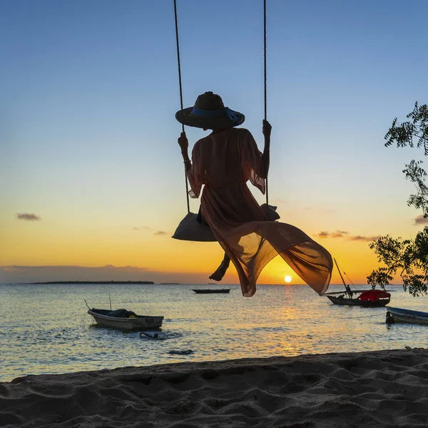 Afrika, Tanzanya 'daki Zanzibar Adası' nın batışında plajda salıncakta sallanan hasır şapkalı ve pareolu güzel bir kız. Seyahat ve tatil kavramı — Stok fotoğraf