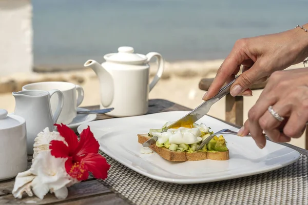 Sanduíche saudável com abacate, pepino e ovos escalfados na mesa para um pequeno-almoço saudável na praia perto do mar. Conceito de comida e pequeno-almoço . — Fotografia de Stock