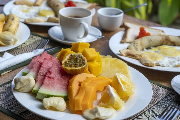 Тропічний сніданок з фруктами, кавою та яєчнями та банановою млиною на двох на пляжі біля моря — стокове фото