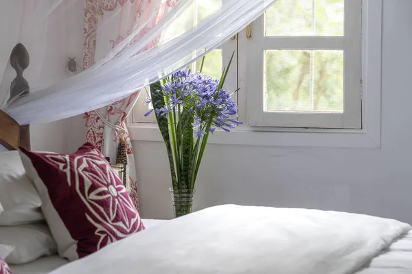 Lit douillet confortable dans la chambre et un bouquet de fleurs près de la fenêtre, gros plan — Photo