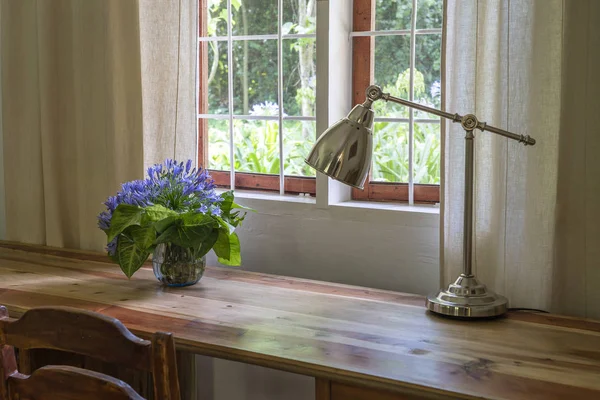 Mesa de madera con silla, lámpara y un ramo de flores cerca de la ventana en el área de trabajo moderna en casa —  Fotos de Stock