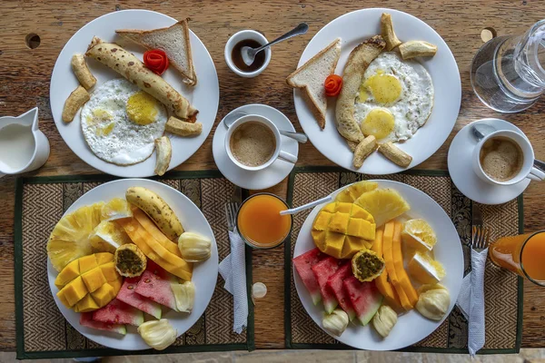 Тропический завтрак из фруктов, кофе, яичницы и бананового блина на двоих на пляже у моря — стоковое фото