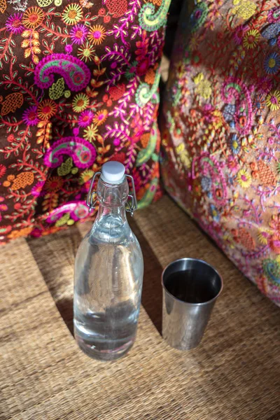 Wasserflasche auf Holztisch mit buntem Kissenhintergrund im indischen Café — Stockfoto