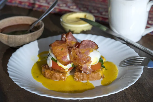 Pastırmalı Benedict usulü yumurta, kızarmış ekmek ve domates, yakın plan. Kahvaltıda haşlanmış yumurtalı sandviç. — Stok fotoğraf