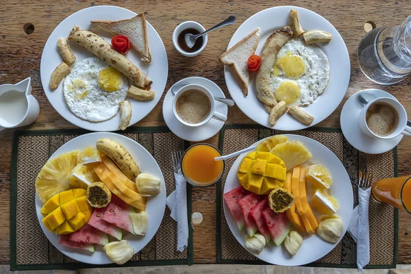 Desayuno tropical de frutas, café y huevos revueltos y tortitas de plátano para dos personas en la playa cerca del mar — Foto de Stock