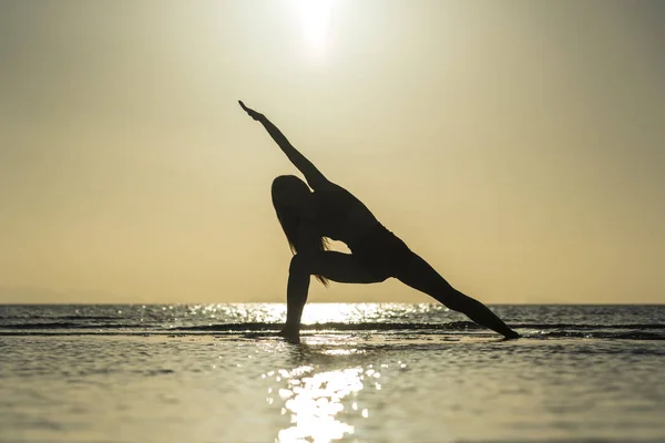 Silhouette of woman standing at yoga pose on the tropical beach during sunset. Girl practicing yoga near sea water — Stock Photo, Image