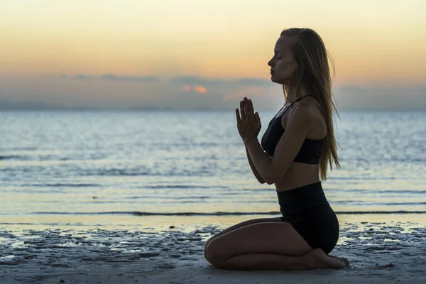 Silhouette of woman sitting at yoga pose on the tropical beach during sunset. Girl practicing yoga near sea water — Stok fotoğraf