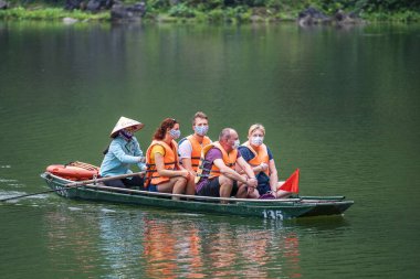 Ninh Binh, Vietnam - march 1006, 2020 : Tourist boat trip on river in Trang An Hang Mua, Vietnam. People with protective mask on the face. Coronavirus outbreak prevention in public area