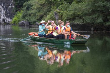 Ninh Binh, Vietnam - march 1006, 2020 : Tourist boat trip on river in Trang An Hang Mua, Vietnam. People with protective mask on the face. Coronavirus outbreak prevention in public area