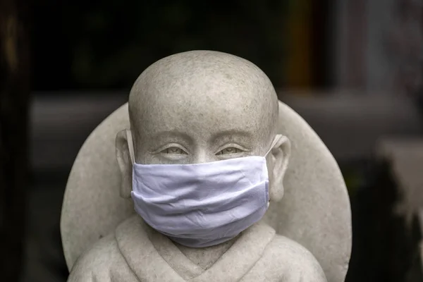 Portrait of buddhist statue wearing a face mask, close up. Concept flu epidemic, coronavirus, dust allergy, protection against virus. White protective mask against coronavirus on a buddhist statue