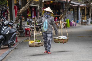 Hoi An, Vietnam - 16 Mart 2020: hasır şapkalı Vietnamlı kadın Hoi An, Vietnam 'da eski bir şehirde bir sepet meyveyle sokak pazarında