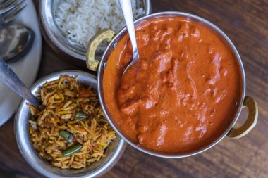 Navratan safranlı biryani taze sebze, baharat ve basmati pilavı metal bir tencerede ve ahşap arka planda kırmızı köri soslu tavuk parçaları, üst manzara, yakın çekim. Hint mutfağı