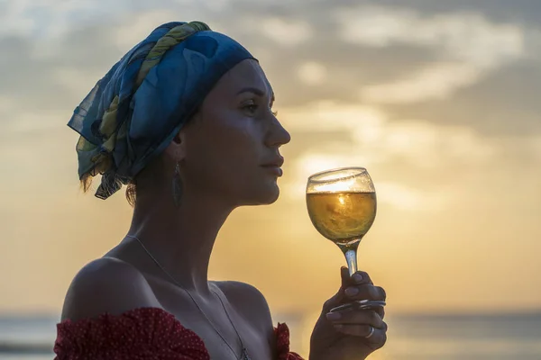热带海滩上 一个可爱的女人在海浪边 面对美丽的落日 举着一杯白葡萄酒 女孩正在喝着一杯葡萄酒欣赏日落 休闲和旅行的概念 — 图库照片