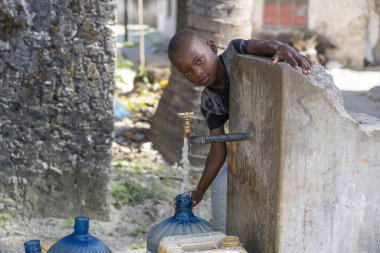 Zanzibar, Tanzanya - 29 Ekim 2019: Tanzanya, Doğu Afrika 'daki Zanzibar Adası' ndaki bir sokakta kimliği belirsiz Afrikalı çocuk teneke kutuyu musluk suyuyla doldurdu