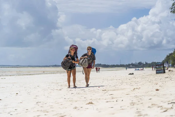 タンザニアのザンジバル 12月12 2019 砂浜にバックパックを持つ2人の女の子観光客は 東アフリカタンザニアのザンジバル島で無料の住宅を探しています — ストック写真