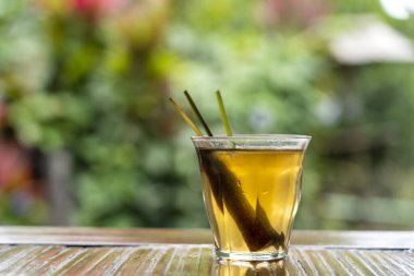 Sağlıklı, ferahlatıcı bir tarçın içeceği ve tropik bir bahçedeki ahşap bir masada limon otu sapları. Kapat.