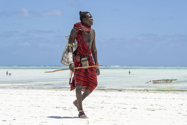Zanzibar, Tanzania - november 11, 2019 : African man masai dressed in traditional clothes standing near the ocean on the sand beach of Zanzibar island, Tanzania, East Africa