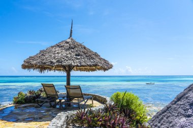 Güneşli bir günde, Zanzibar, Tanzanya, Doğu Afrika 'da deniz kenarındaki tropikal bir plajda saman şemsiyesi ve iki tahta güneşlik.