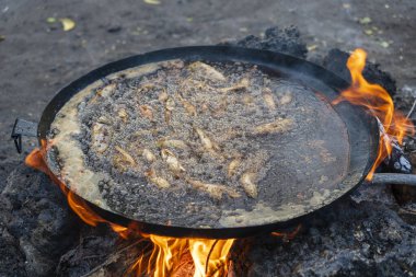 Satıcı, Doğu Afrika 'daki Tanzanya' nın Zanzibar adasındaki yerel bir sokak gıda pazarında büyük bir kızartma tavasında sebze yağında balık kızartıyor. Kapat.