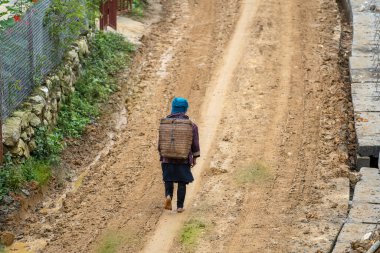 A barefoot ethnic Hmong woman walks along a dirt road after rain on the street in mountain village Sapa, North Vietnam clipart